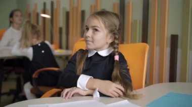 Kendine güvenen küçük beyaz kız ders sırasında öğretmenlerin sorularına cevap vermek için elini kaldırıyor. Devlet okulunda okuyan zeki öğrencilerin portresi. Eğitim kavramı.