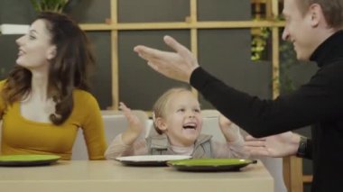 Neşeli beyaz adam, kadın ve kız restoranda oturmuş lezzetli taze pizza getiriyorlar. Mutlu kız ve ebeveynler pizzacıda yemek yerken gülümsüyor ve konuşuyorlar..