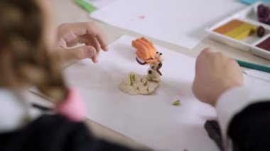 Masada kilden heykel yapan bir kız öğrencinin omzundan ateş etmek. Tanımlanamayan beyaz bir kız okuldaki sanat dersinde plastikçilik yapıyor. Yaratıcılık ve eğitim kavramı.