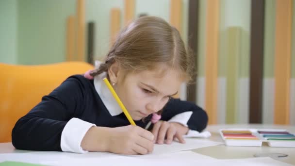 Porträtt av olycklig flicka rita vid skrivbordet och kasta penna. Söt liten vit skolflicka som har problem med konst lektion i allmän skola. Utbildning och studier. — Stockvideo