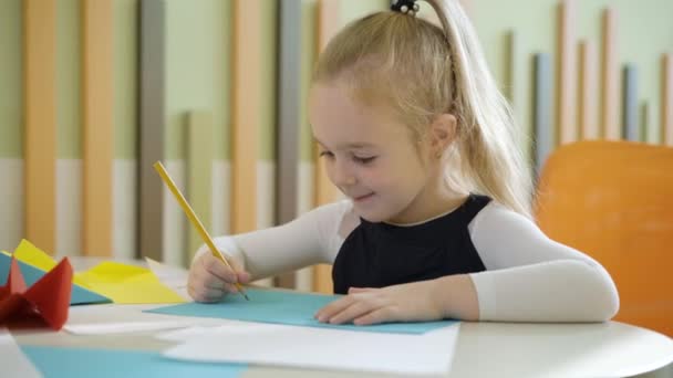 Urocza blond biała dziewczyna rysunek ołówkami siedzi przy stole w przedszkolu lub szkole. Portret szczęśliwej uczennicy w wieku podstawówki obraz malarski i uśmiech. Dzieciństwo i edukacja. — Wideo stockowe