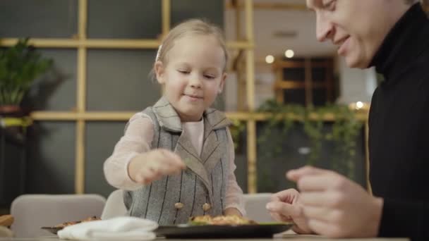 ピザからオレガノを食べる喜びの美しい白人の女の子と巨大な笑顔の幸せな男.父親と一緒にピッツェリアレストランで休んでいる陽気な娘の肖像画。レジャーとライフスタイル. — ストック動画