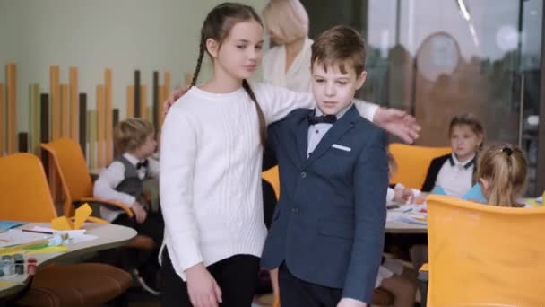 Belle fille et beau garçon embrassant et agitant à la caméra dans la salle de classe. Portrait d'heureux écoliers caucasiens posant à l'école publique. Concept d'éducation et d'amitié. — Video