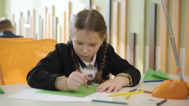 Skoncentrowany cute uczennica rysunek podczas przerwy. Portret skupionej białej dziewczynki siedzącej przy stole w szkole publicznej i malującej ołówkami. Koncepcja edukacji i kreatywności. — Wideo stockowe
