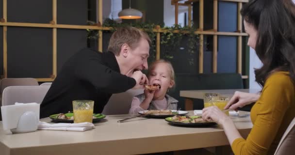 Cheerful father and daughter having fun fighting for pizza slice in restaurant. Happy mother admiring family eating delicious dish in pizzeria. Cinema 4k ProRes HQ. — Stock Video