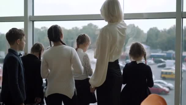 Baksidan av lärare och skolbarn tittar ut genom fönstret och pratar. En grupp söta kaukasiska pojkar och flickor som chattar med handledare i den offentliga skolan. Undervisnings- och studiebegreppet. — Stockvideo