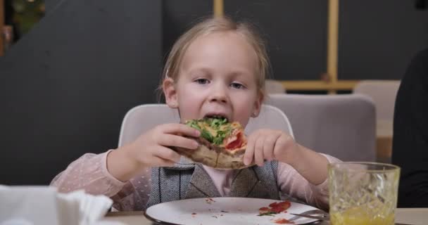 Nahaufnahme eines charmanten kleinen Mädchens, das im Restaurant Pizza beißt und kaut. Porträt eines süßen kaukasischen Kindes, das in einer Pizzeria im Haus leckere Gerichte isst. Food-Konzept. Cinema 4k ProRes Hauptquartier. — Stockvideo