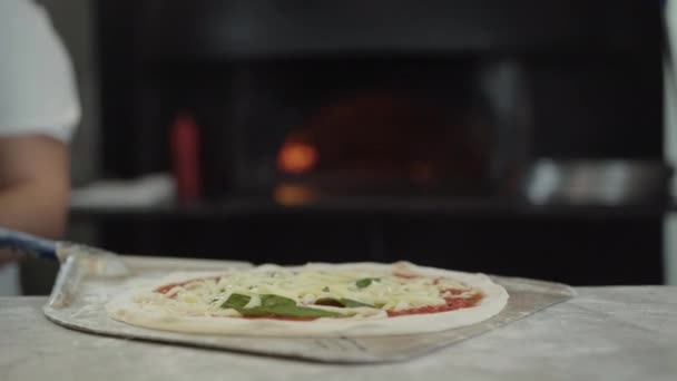 Close-up van rauwe pizza op het koken schop met onherkenbare kok zet het in de oven in de keuken. Professionele Kaukasische chef kokend smakelijk Italiaans gerecht in restaurant of pizzeria. — Stockvideo