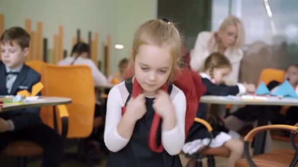 Ritratto di affascinante bella studentessa bionda con gli occhi grigi in posa in classe. Positivo carino ragazza caucasica guardando la fotocamera e sorridendo con insegnante offuscata e compagni di classe sullo sfondo. — Video Stock