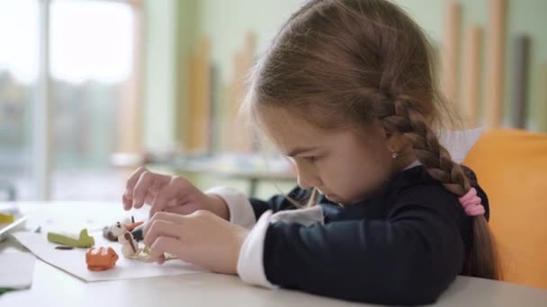 Side view close-up van geconcentreerde schoolmeisje modelleren klei op bureau op school op kunstles. Gericht mooie brunette Kaukasisch meisje studeren binnen. Vertrouwen en creativiteit. — Stockvideo