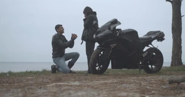 在多云的河岸上，一个快乐的男朋友向她求婚的全景。订婚后，一对快乐的跨种族自行车手在户外拥抱。Cinema 4k ProRes HQ. — 图库视频影像
