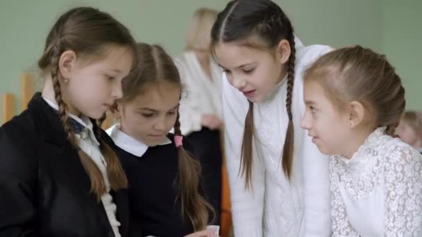 Gros plan de quatre écolières bavardant avec un professeur flou parlant en arrière-plan. Mignonnes filles caucasiennes partageant des secrets et parlant en classe à l'école publique pendant la pause. Concept d'amitié. — Video