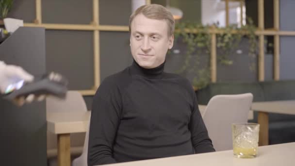 Hombre caucásico seguro que paga en el restaurante con un teléfono inteligente. Retrato de joven hombre de negocios guapo haciendo el pago inalámbrico sin efectivo en la cafetería. Tecnologías modernas y estilo de vida. — Vídeo de stock