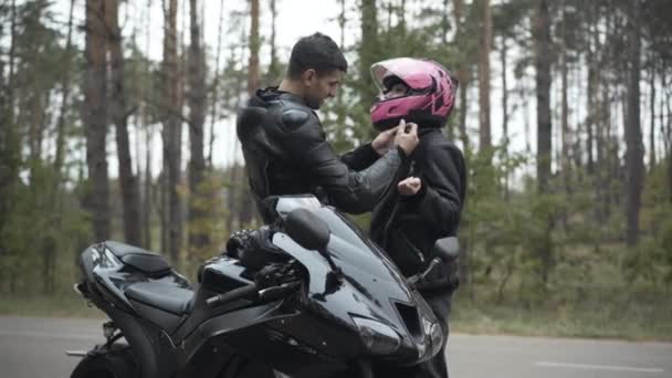 Liebevoll lächelnder Biker aus dem Nahen Osten, der Freundinnen im Freien einen rosafarbenen Helm aufsetzt. Schöner Freund kümmert sich um schöne kaukasische Frau. Interrassische Beziehung und Rennkonzept. — Stockvideo