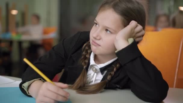 Närbild av uttråkad geni skolflicka sitter vid bordet i klassrummet och rita. Porträtt av en söt vit flicka som studerar i folkskolan. Intelligens och tristess koncept. — Stockvideo