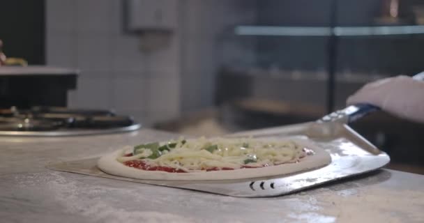 Primer plano de la pizza cruda en la pala de cocina en la cocina del restaurante. Chef caucásico irreconocible tomando plato para horno. Proceso de hacer pizza en interiores. Sede del cine 4k ProRes. — Vídeo de stock