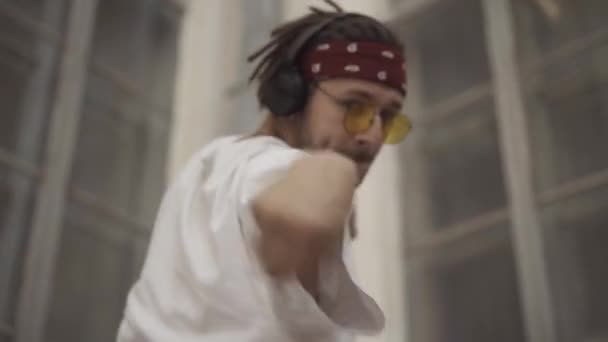 Zoom aus selbstbewussten jungen Breakdancern, die in städtischen Slums auftreten. Porträt eines kaukasischen Hippie-Mannes mit Sonnenbrille und Dreadlocks, der draußen vor der Kamera tanzt. — Stockvideo