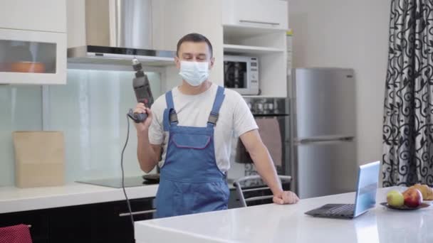 Positive confident repair man in Covid-19 face mask posing with electric tool in apartment. Young Caucasian worker fixing breakage on coronavirus pandemic. Professionalism concept. — Stock Video