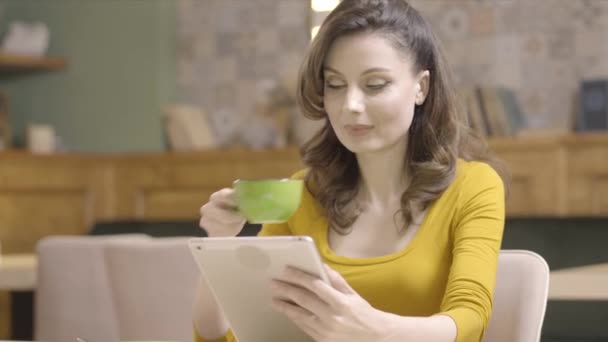 Confident beautiful young woman drinking tea or coffee and using tablet in cafe or restaurant. Portrait of happy Caucasian charming lady resting indoors. Leisure and lifestyle confidence. — Stock Video