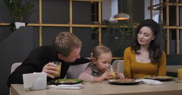 Gelukkige paar ouders bewonderen leuke charmante dochter drinken sinaasappelsap en praten. Portret van een lachende mooie vrouw en knappe man die dineert met een kind in de pizzeria. Cinema 4k ProRes Hoofdkwartier. — Stockvideo