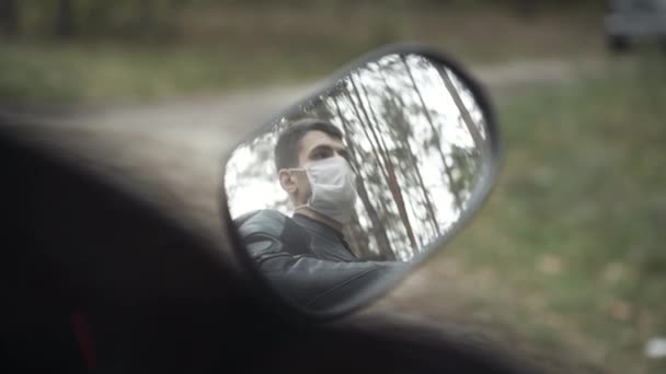 Reflection in motorcycle rear view mirror of handsome confident Middle Eastern man in Covid-19 face mask. Young brunette motorcyclist sitting on motorbike during coronavirus pandemic lockdown. — Stock Video