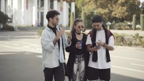 Relaxed millennial Caucasian friends with tattoos and piercings walking outdoors talking. Portrait of positive young men and woman chatting on sunny day in city. Friendship and lifestyle concept. — Stock Video
