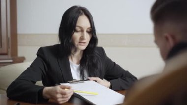 Beyaz kadın psikolog, üzgün yüzünü kâğıda döküyor ve ofisteki bulanık adamla konuşuyor. Sinir krizi geçiren kendine güvenen profesyonel bir kadının portresi..