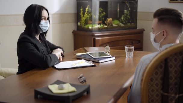 Retrato de vista lateral del psicólogo y paciente en Covid-19 mascarillas tocando codos al final de la consulta. Hombre y mujer caucásicos reemplazando apretón de manos en pandemia de coronavirus. — Vídeos de Stock