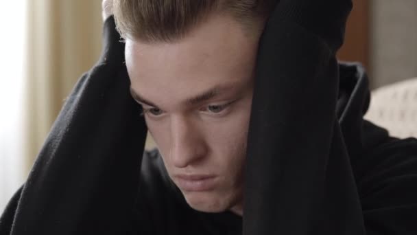 Detailní záběr frustrovaného mladíka, který drží hlavu v dlaních a přemýšlí. Portrét zoufalého bělocha v kanceláři psychologa. Koncept zoufalství a deprese. — Stock video