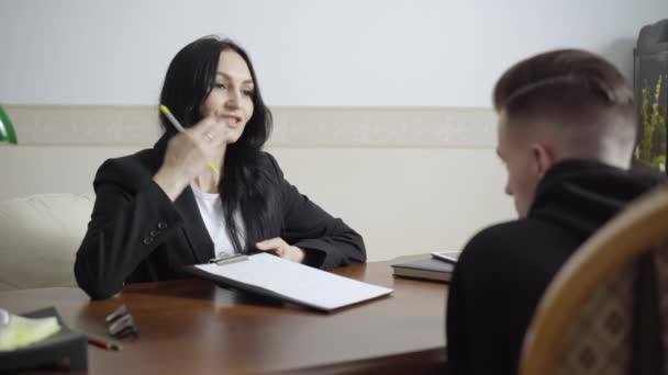 Professioneller Psychologe im Gespräch mit einem Patienten im Amt, der ein trauriges Gesicht zu Papier bringt. Porträt einer selbstbewussten kaukasischen Frau, die einen Mann im Haus berät. Psychologische Unterstützung und Stressabbau-Konzept. — Stockvideo