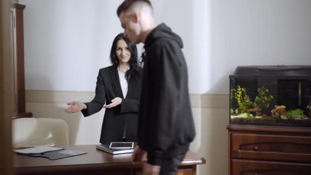 Psicólogo profesional positivo acogiendo al paciente en consultorio. Retrato de una joven mujer caucásica sonriendo y hablando con un hombre deprimido en el interior. Concepto de ayuda psicológica. — Vídeo de stock