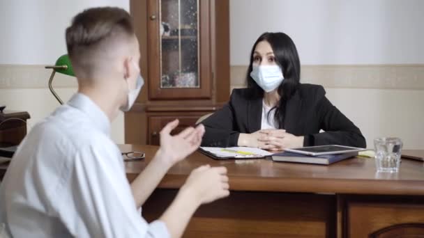 Femme caucasienne de soutien dans le masque facial Covid écouter l'homme stressé parler assis dans le bureau de psychologue. Professionnel femme spécialiste consultation désespérée jeune patient sur le confinement pandémique. — Video