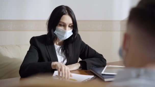 Retrato de psicólogo profesional en máscara facial Covid consultando al paciente sobre pandemia de coronavirus. Mujer caucásica seria hablando con un hombre desesperado estresado en el interior. Covid-19 crisis nerviosa. — Vídeo de stock