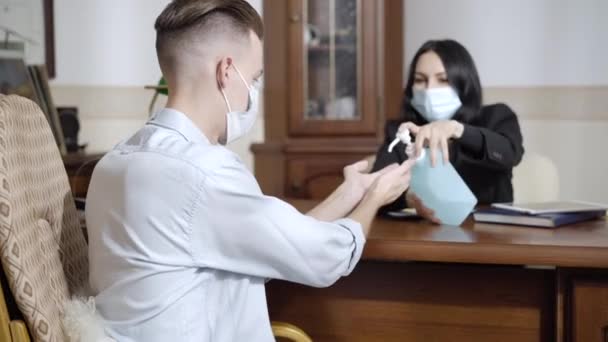 Psychologist on Covid-19 face mask spraying sanitizer on hands of patient indoors. Sad Caucasian man disinfecting palms on psychological consultation. Coronavirus new normal lifestyle. — Stock Video