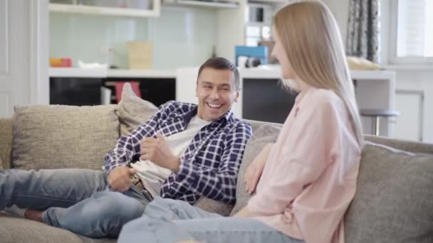 Couple aimant positif s'amuser sur le canapé dans le salon. Heureux homme et femme caucasien joyeux se battant et riant à la maison le week-end. Petit ami joyeux et petite amie à l'intérieur. — Video