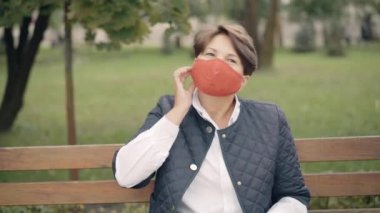 Covid-19 maskesini çıkarıp kameraya gülümseyen güzel bir son sınıf güzeli. Mutlu Kafkasyalı emeklinin portresi Coronavirus salgınının sonundaki bahar ya da sonbahar parkında eğleniyor..