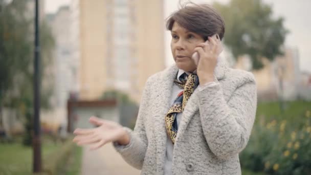 Bella donna anziana che parla al telefono all'aperto. Ritratto di donna caucasica elegante stressata che usa lo smartphone sulla strada della città. Stile di vita e tecnologie moderne. — Video Stock