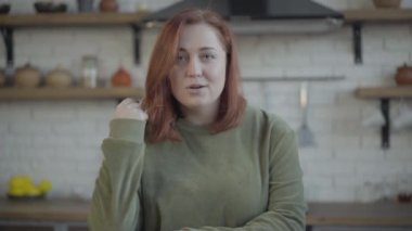 Kızıl saçlı, beyaz bir kadının kameraya bakarken yüzünün aldığı hali. Evdeki mutfakta poz veren neşeli, tombul kadının portresi..