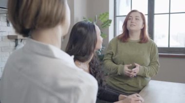 Çekici, iri yarı, kızıl saçlı bir kadın arkadaşının konuşmasını dinliyor ve gülümsüyor. Beyaz kadın portresi. Mutfakta sohbet ediyorlar ya da dedikodu yapıyorlar. Kadın arkadaşlığı kavramı.
