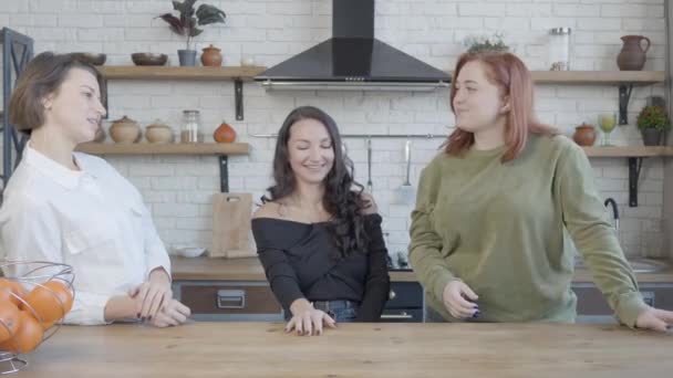Három fiatal pozitív kaukázusi nő beszélget és nevet a konyhában. Boldog, nyugodt női barátok, akik otthon pletykálnak. Barátság és életmód koncepció. — Stock videók