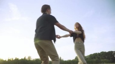 Neşe dolu Kafkasyalı genç çiftin yaz otlaklarında el ele tutuşmalarının alt açısı. Gün batımında eğlenen neşeli kız ve oğlanın geniş açılı görüntüsü. Eğlence ve eğlence..