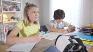 Çalışma kitabına odaklanmış dahi kız portresi ve arka planda bulanık erkek çizimi. Modern sınıftaki masa başında çalışan konsantre, zeki, beyaz çocuklar. Eğitim.