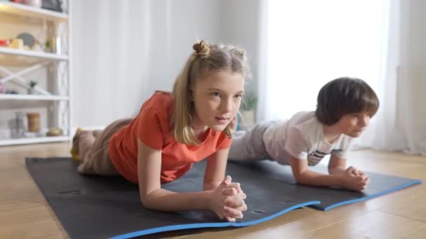 Två koncentrerade passform kaukasiska barn i planka position hemma. Porträtt av självsäker bror och syster som tränar inomhus. Workout och utbildning koncept. — Stockvideo
