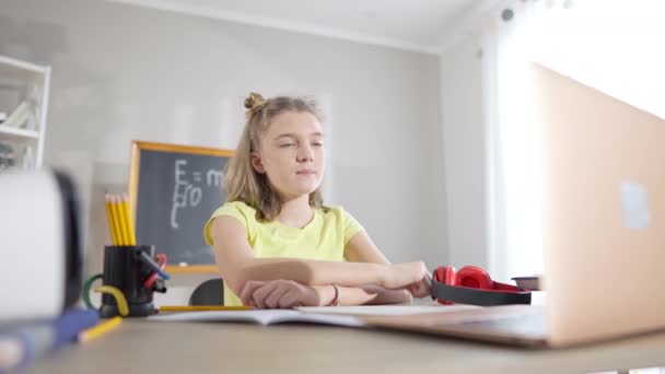 Inteligentna, biała uczennica siedząca przy biurku z podniesioną ręką na laptopie. Portret mądrej pięknej dziewczyny studiującej online na blokadzie pandemii koronawirusowej. Covid-19 nowy normalny styl życia i — Wideo stockowe