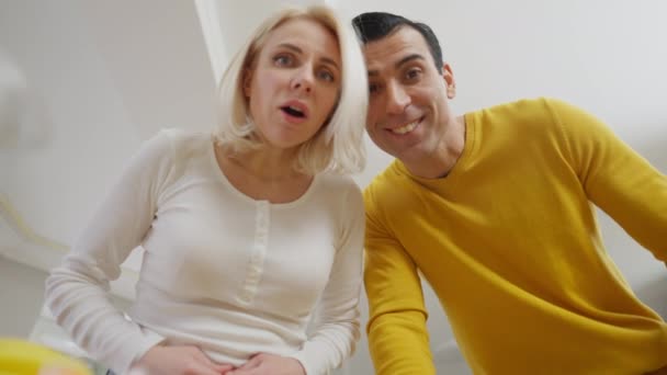 Excited interracial couple throwing green leaves in blender smiling. Bottom view portrait of happy Caucasian young woman and Middle Eastern handsome man preparing smoothie at home. — Stock Video