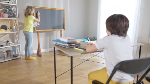 Široký záběr pozitivní sebevědomé školačky, která píše na školní radu jako rozmazaný školák sedící za stolem ve třídě. Geniální běloška rukopis matematický úkol na lekci ve škole. — Stock video
