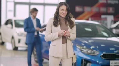 Galeride araba anahtarlarıyla dans eden heyecanlı genç bir kadının portresi. Neşeli beyaz kadın galeride otomobil alıyor gülümsüyor ve kameraya bakıyor. Başarı ve zenginlik kavramı.