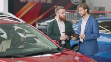 Genç başarılı beyaz iş adamı ve galeride kendine güvenen araba satıcısı sürücü koltuğunda oturan güzel bir kadın gibi konuşuyor. Satıcıdan otomobil alan adam.