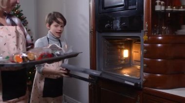 Kafkas anne ve oğlu önlüklü. Evde sebzeli tepsi koyuyorlar. Mutfakta Noel yemeği pişiren pozitif çocuk ve kadın. Yeni yıl kutlaması ve mutfağı.