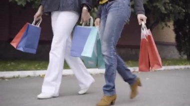 İki ince, şık beyaz kadının alışveriş torbalarıyla dışarı çıkışının yan açısı. Alışverişçilerin asfalt yolda alışverişle dolaştığına eminim. Alışveriş ve yaşam tarzı..